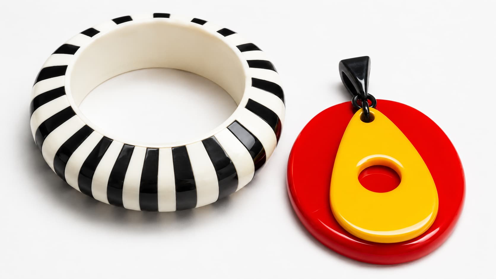Black and white striped Op Art bangle next to a red and yellow Pop Art pendant, 1960s jewelry style