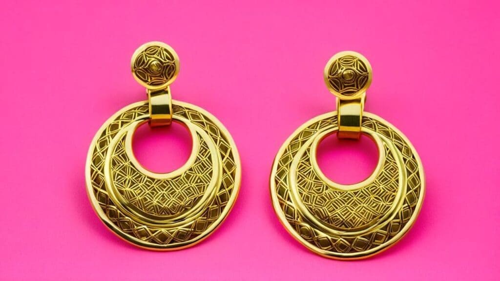 Classic 1980s gold door-knocker earrings with geometric pattern detail against pink background, exemplifying the bold statement jewelry trend of the decade