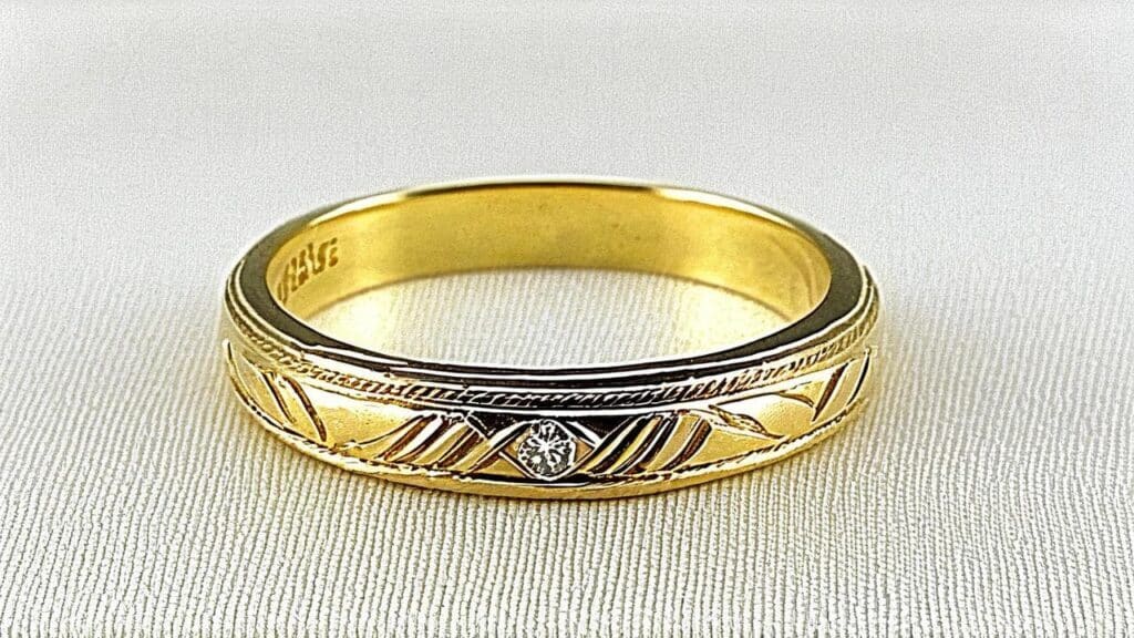 Gold wedding band with engraved pattern and small diamond, representing the sentimental jewelry that took on deeper meaning during wartime separations between couples