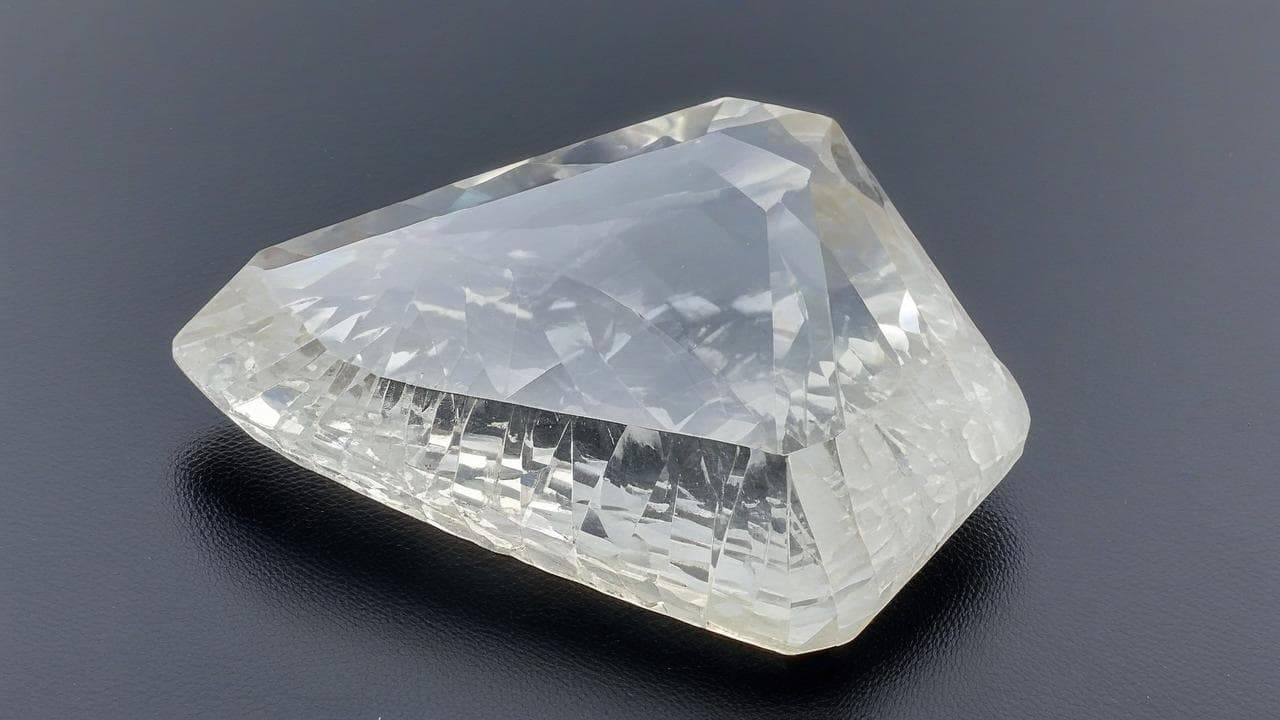 Large fancy-cut colorless barite gemstone on a dark surface