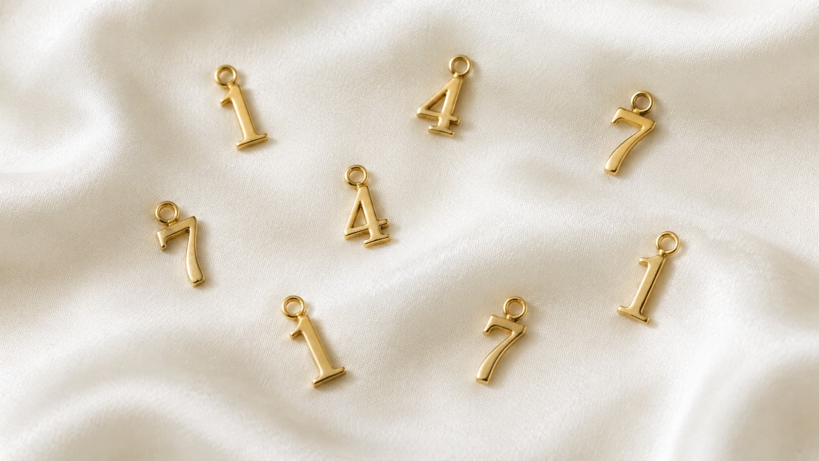 Gold numeral charms shaped like 1, 4, and 7 scattered on white silk fabric