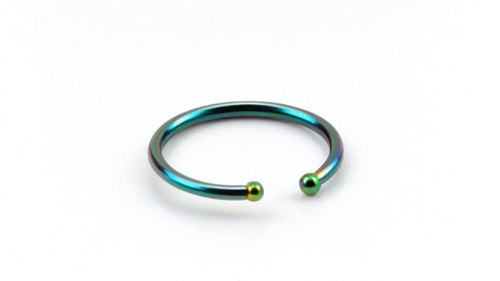 A close-up of an open anodized niobium nose ring with green and blue hues, designed for sensitive skin and body piercings.