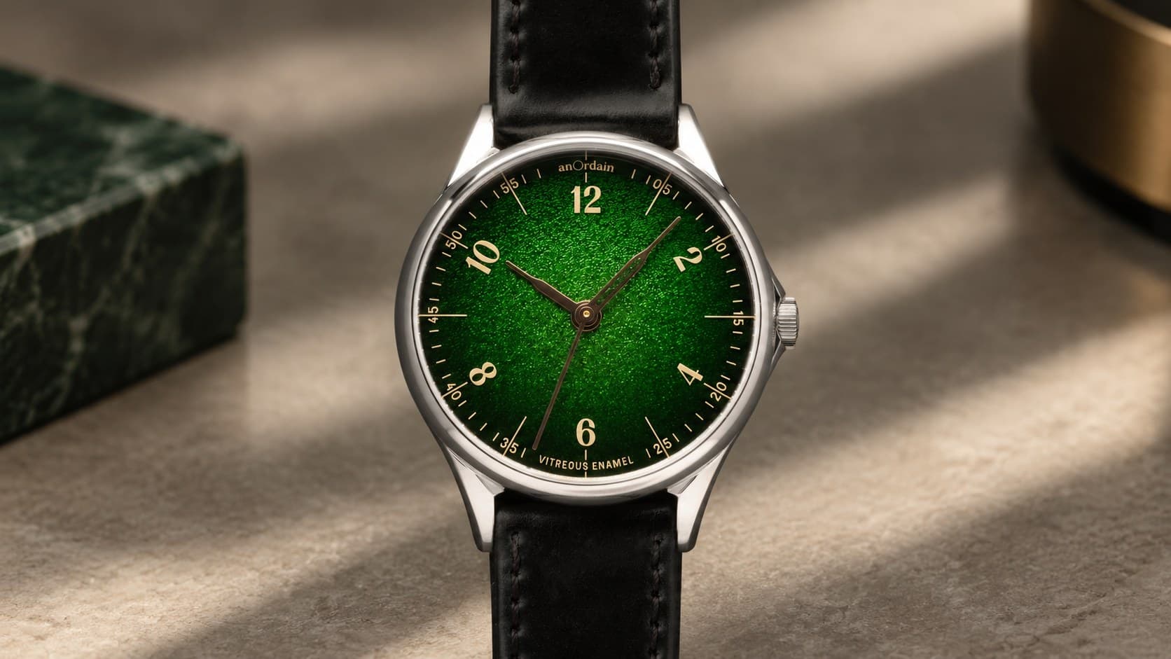 anOrdain Model 1 Fumé watch with a green vitreous enamel dial and black leather strap on a stone surface beside green marble