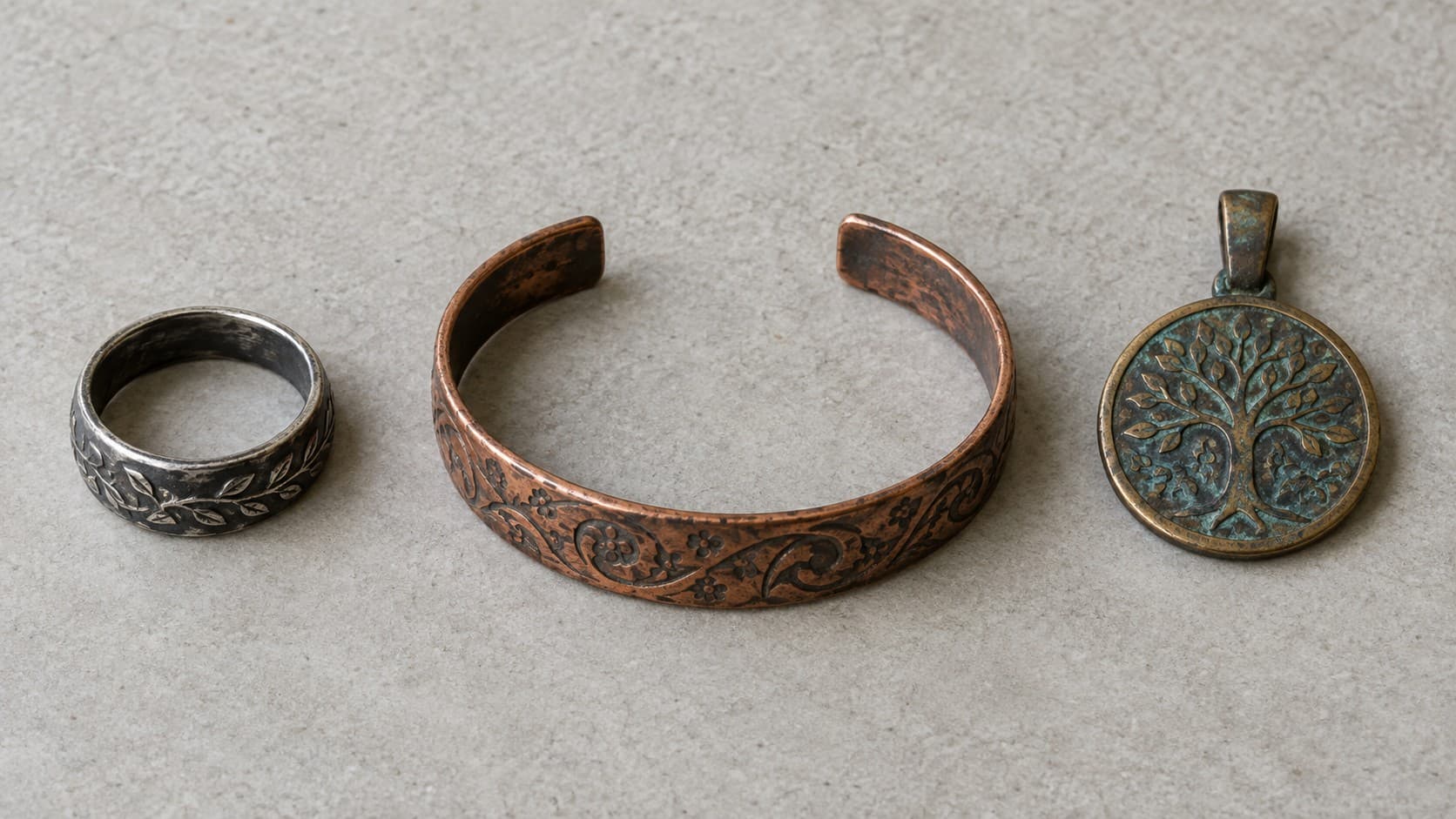 Antiqued sterling silver ring, copper cuff bracelet, and bronze tree of life pendant with natural patina side by side