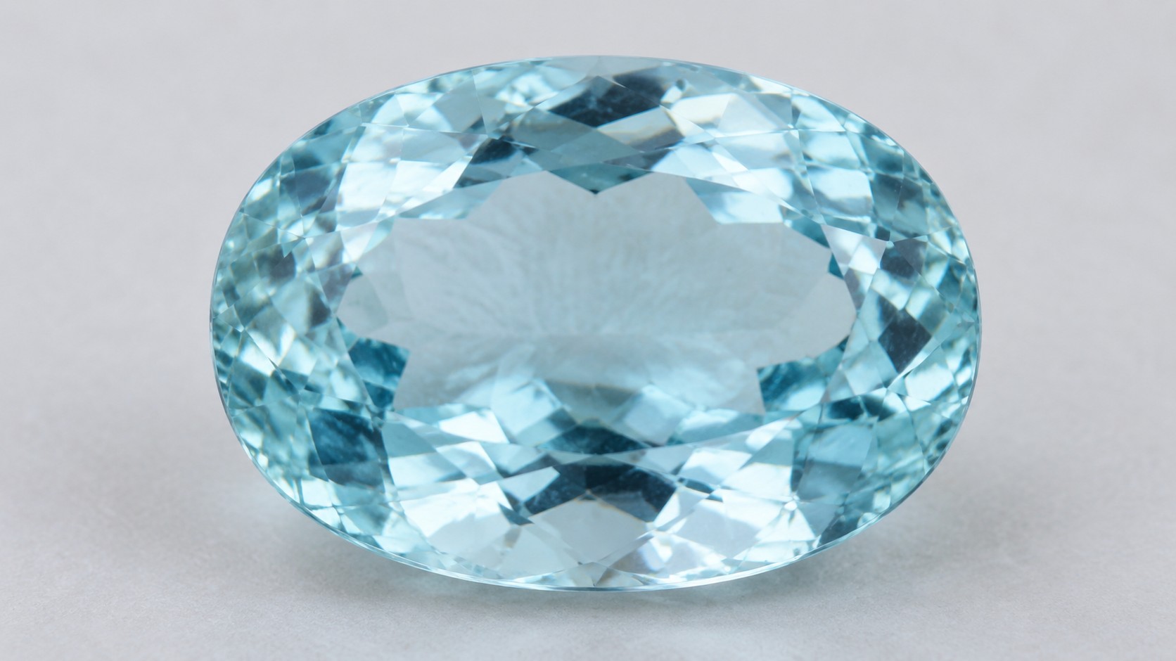Faceted pale blue aquamarine gemstone on a neutral background