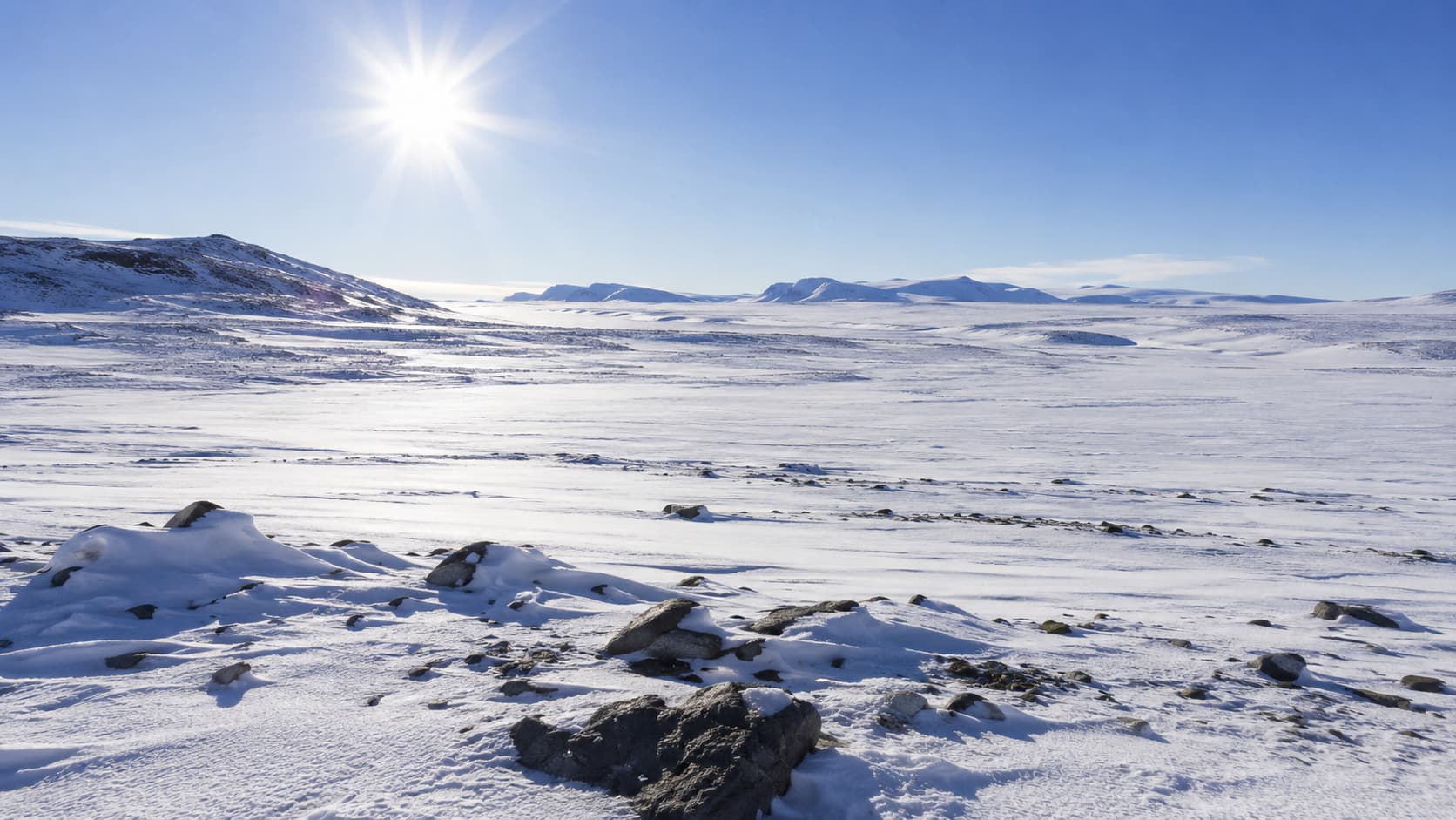 Bright sun glaring off a snow-covered Arctic tundra landscape