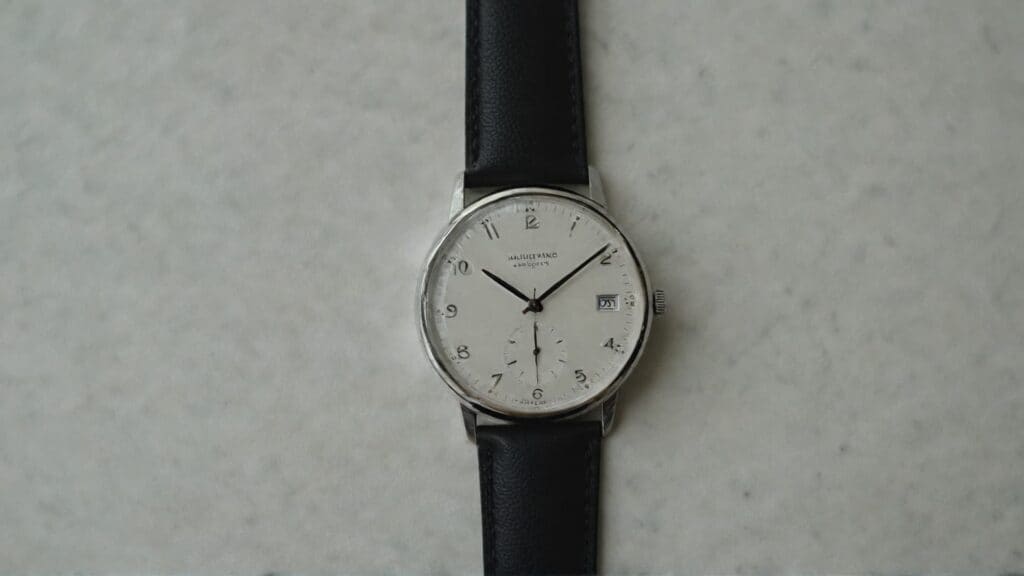 Classic Bauhaus dress watch with white dial, small seconds subdial at 6 o'clock, date window, and black leather strap showing minimalist elegance