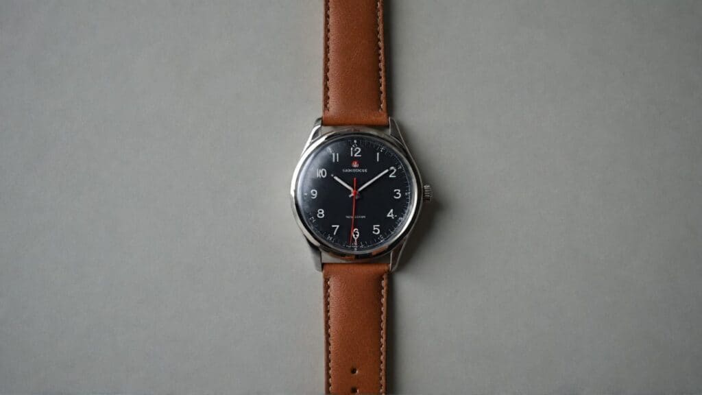 Bauhaus-style watch with black dial, white Arabic numerals, red second hand, and brown leather strap showcasing minimalist design principles