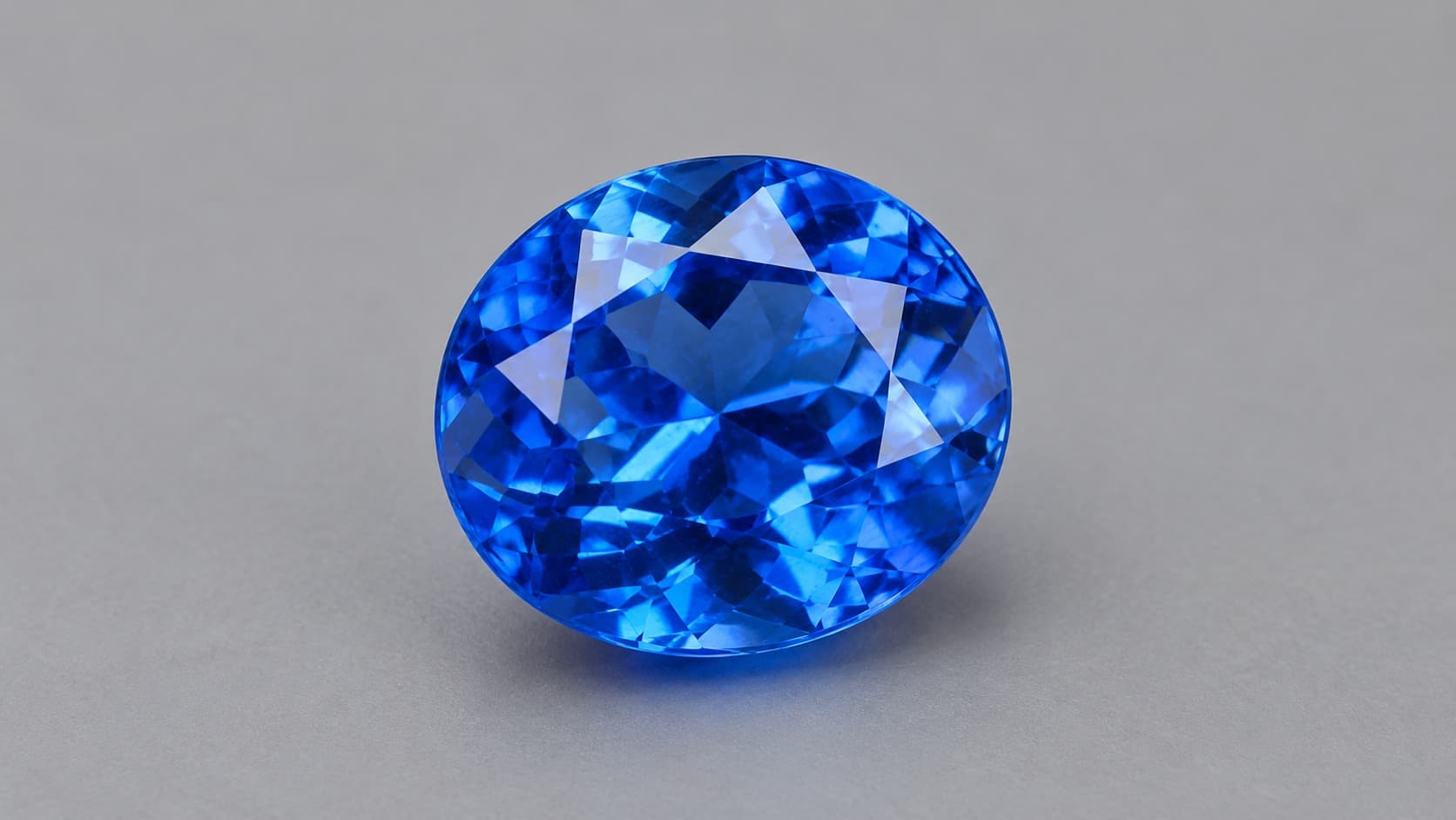Faceted bright blue benitoite gemstone on a neutral gray background