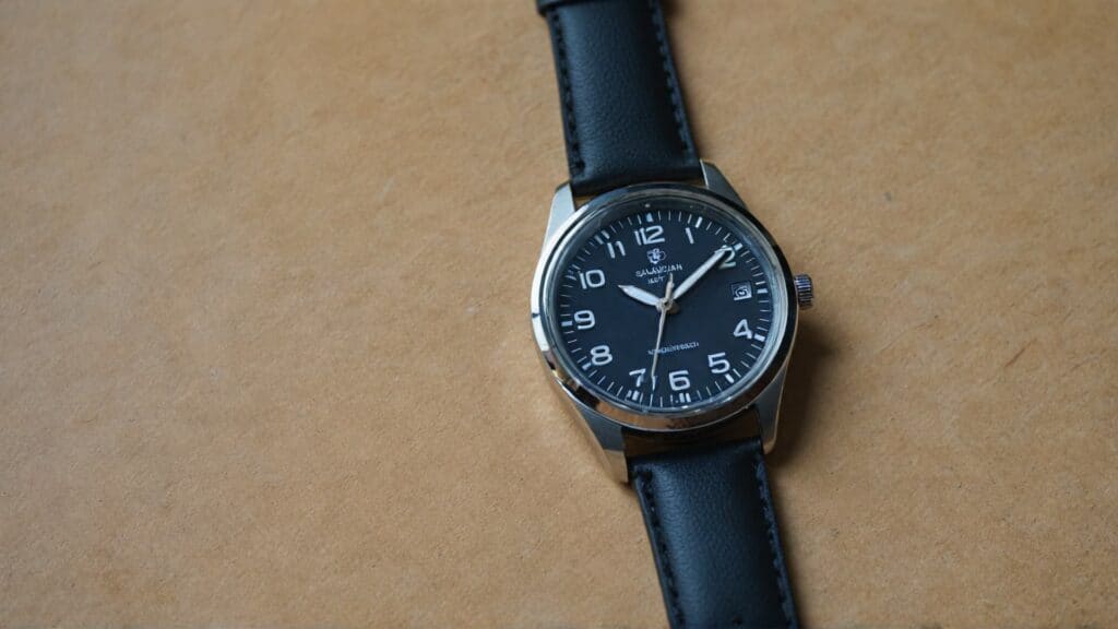 Black dial quartz watch with stainless steel case and black leather strap displaying white Arabic hour markers and date window