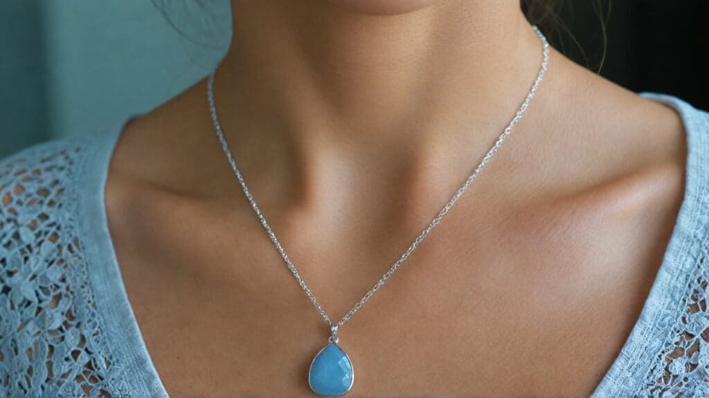 A close-up of a woman wearing a silver chain necklace with a teardrop-shaped blue calcite pendant.