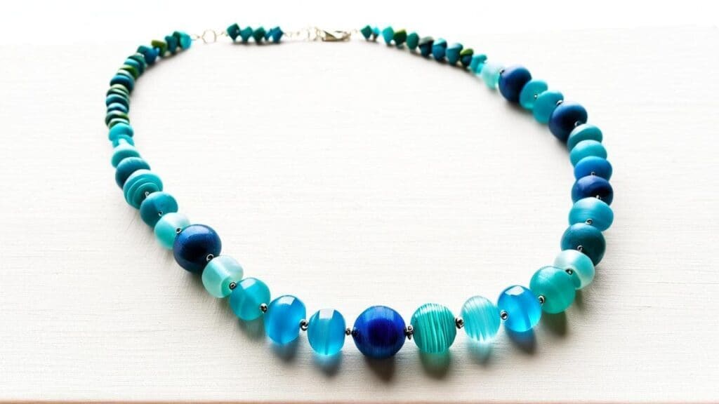 Graduated plastic beaded necklace in shades of blue and teal, featuring translucent and opaque beads in various sizes and textures.