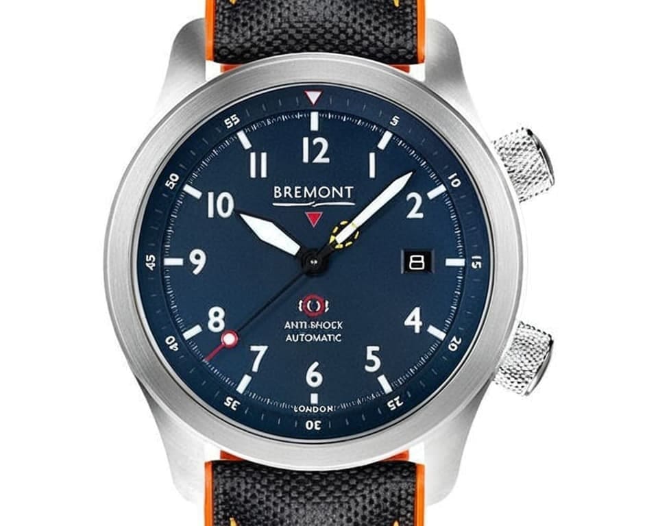 Bremont anti-shock field watch featuring blue dial with Arabic numerals, steel case, orange accent strap, and London marking showing automatic movement and shock resistance