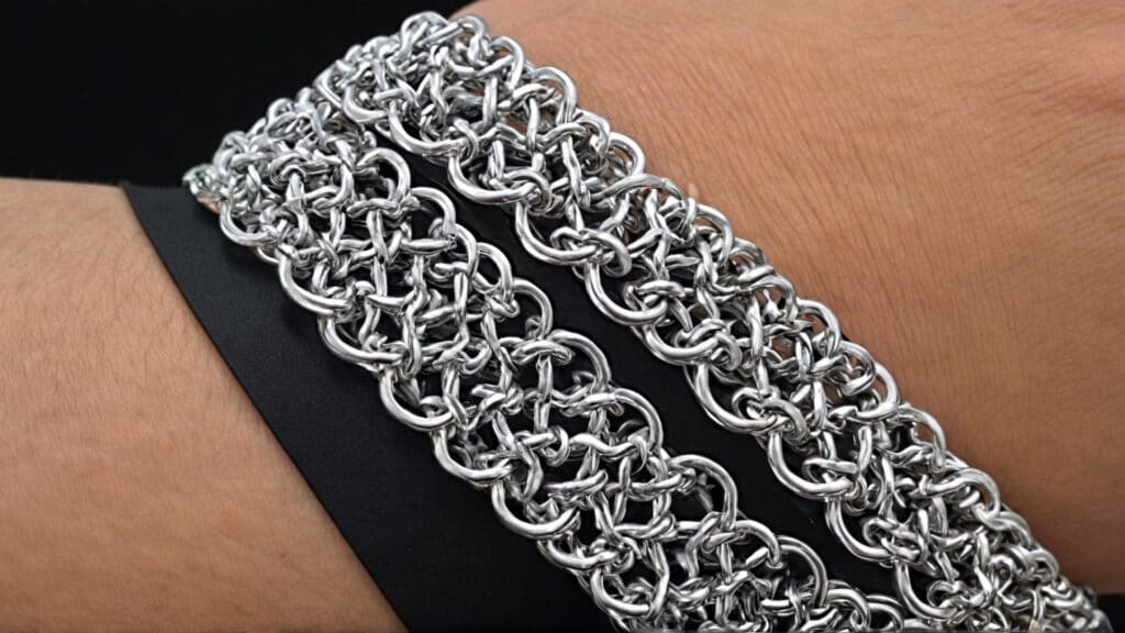 Close-up of a wrist adorned with multiple wide stainless steel chainmaille bracelets, highlighting the complex weave patterns and polished finish.