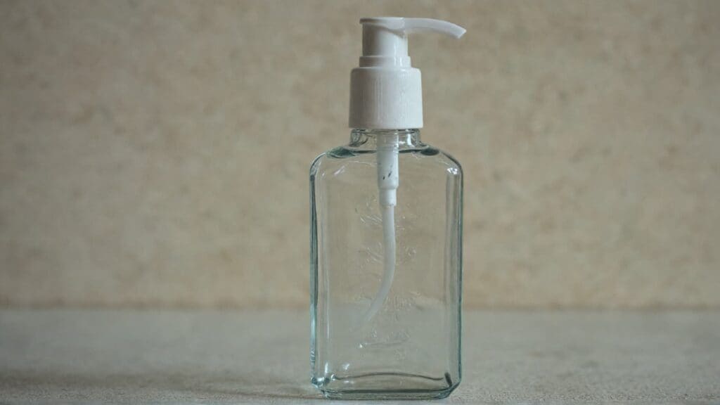 Clear glass hand sanitizer bottle with white pump dispenser on neutral background representing sanitizer products discussed in ring protection guide