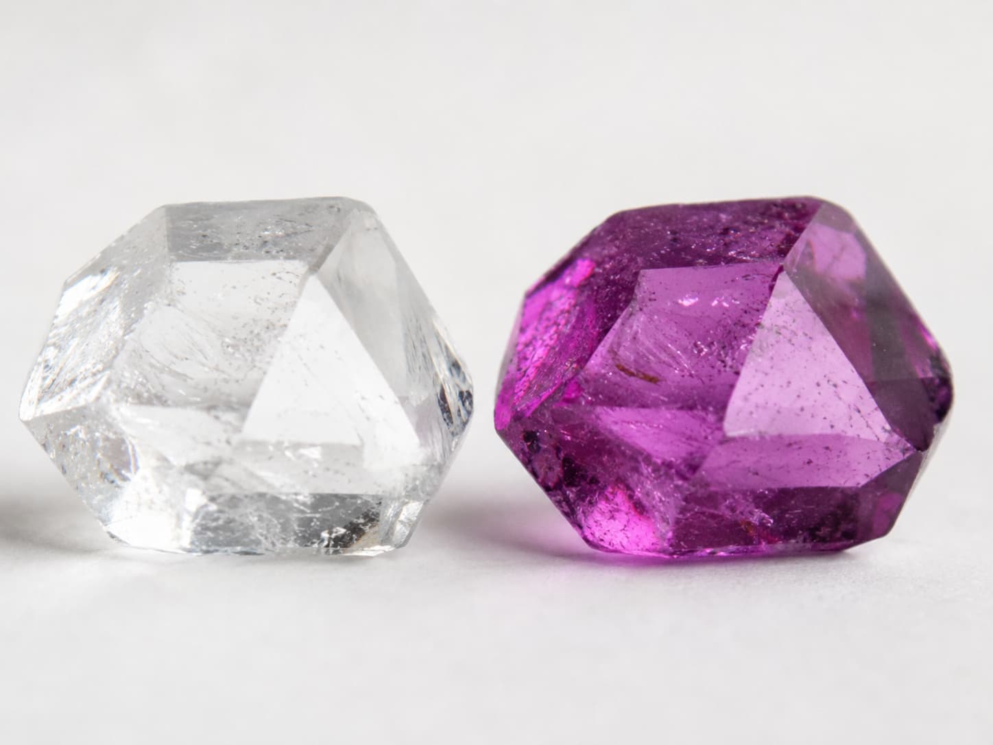 Colorless gemstone crystal next to a colored gemstone crystal of the same mineral