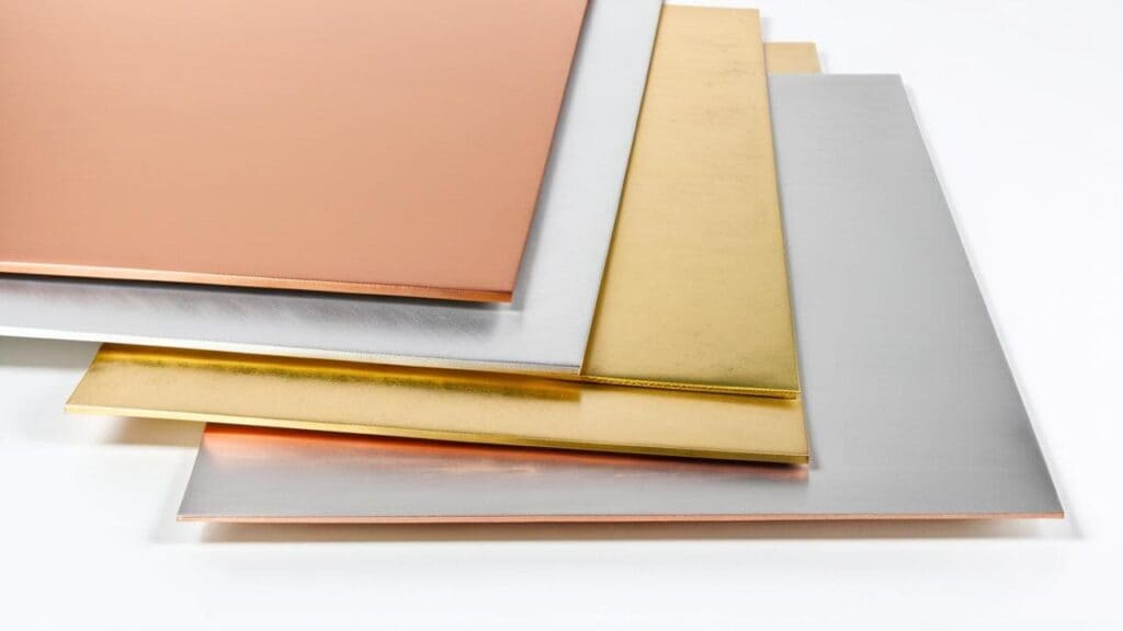 A stack of copper, silver, and gold metal sheets used in jewelry making, each requiring specific annealing temperatures for proper workability.