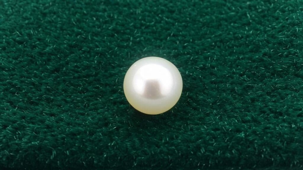 Single cultured pearl with smooth surface and natural luster on dark green fabric background.