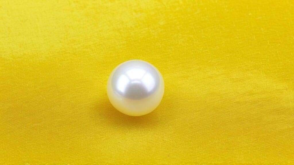 Close-up of a cultured pearl with bright reflective surface on vibrant yellow fabric background.
