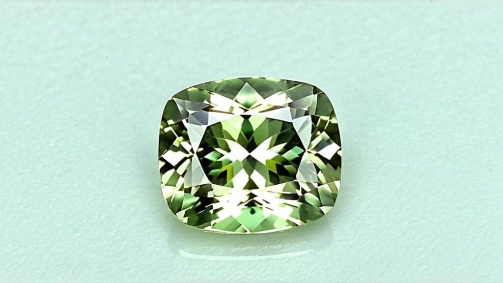 A cushion-cut green sillimanite gemstone with excellent clarity and precise faceting, displayed on a light surface.