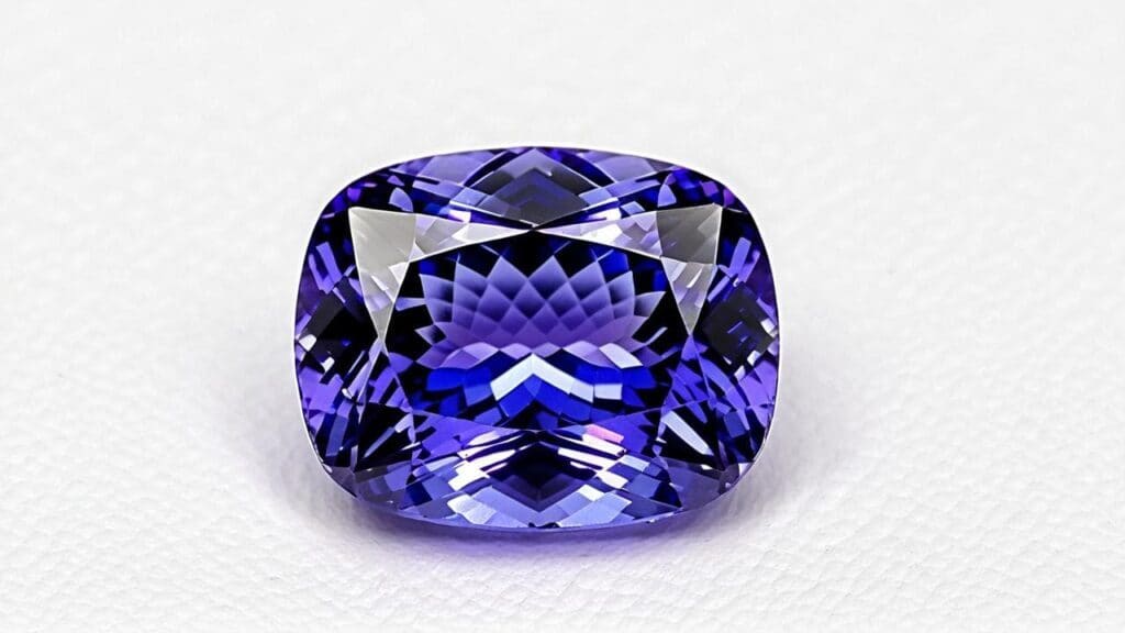 Cushion-cut tanzanite gemstone with deep violet-blue hues and precision faceting on a white background