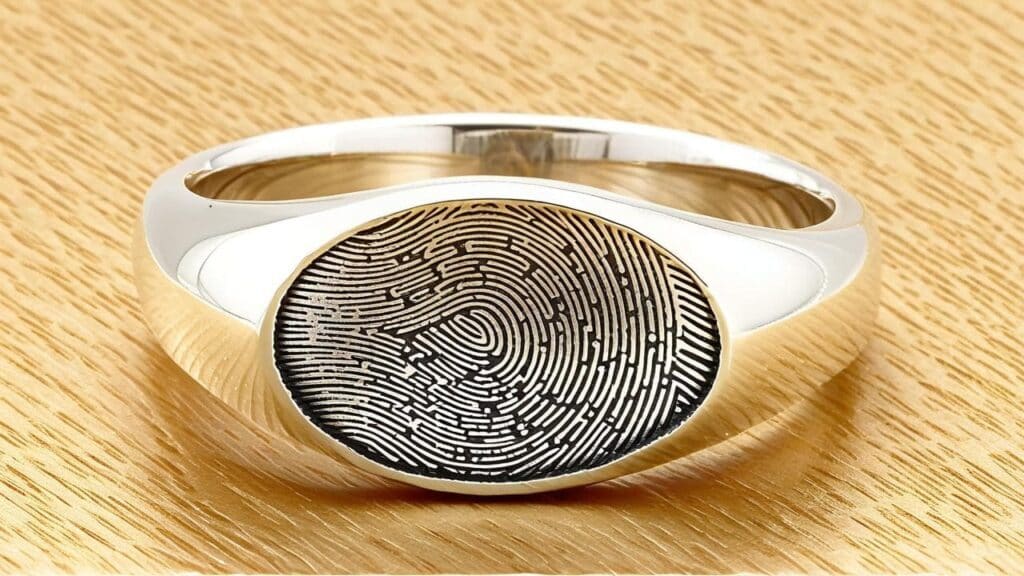 Polished silver signet ring with engraved fingerprint detail on wood background, used as custom memorial jewelry