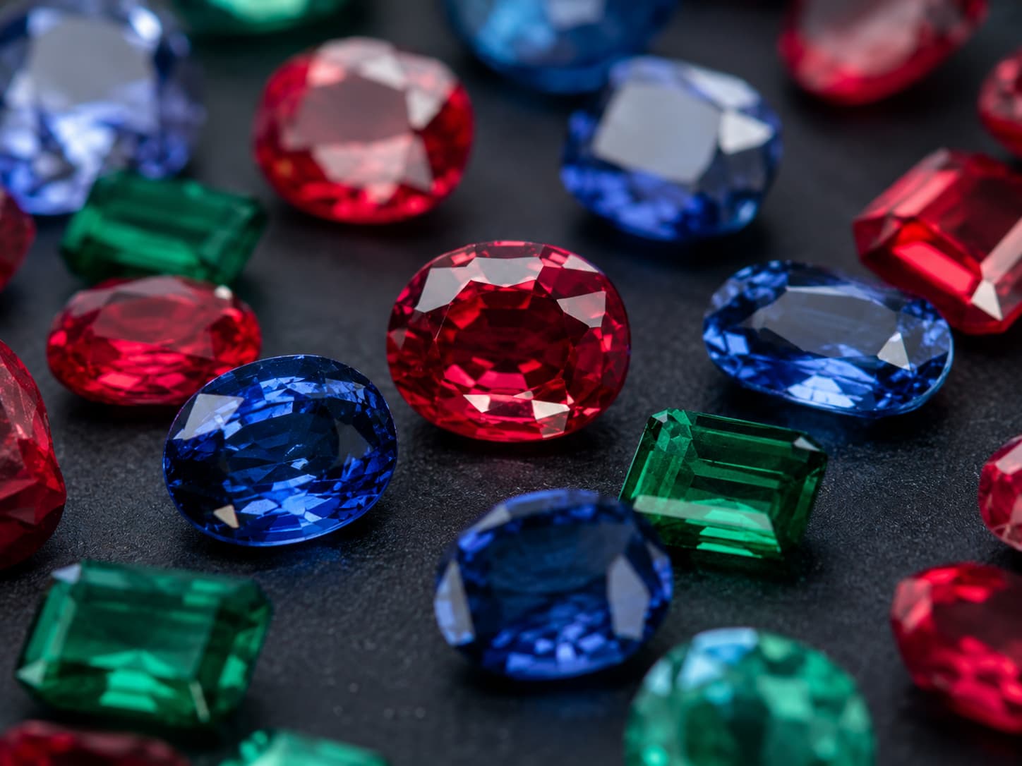 Cut ruby, sapphire, and emerald gemstones arranged together showing vivid color