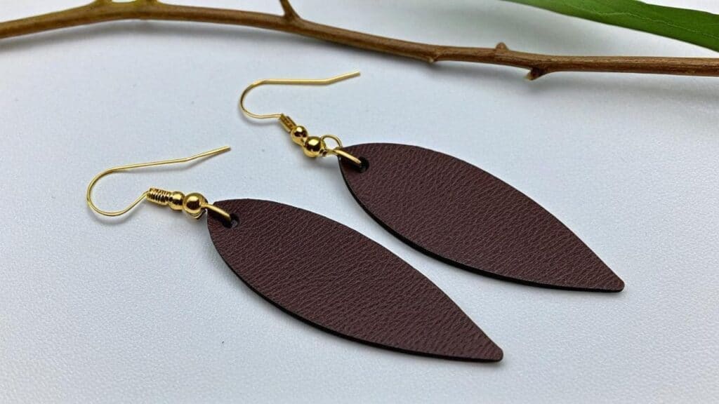 Modern brown leather leaf-shaped statement earrings with gold hooks on white background showcasing natural leather grain texture