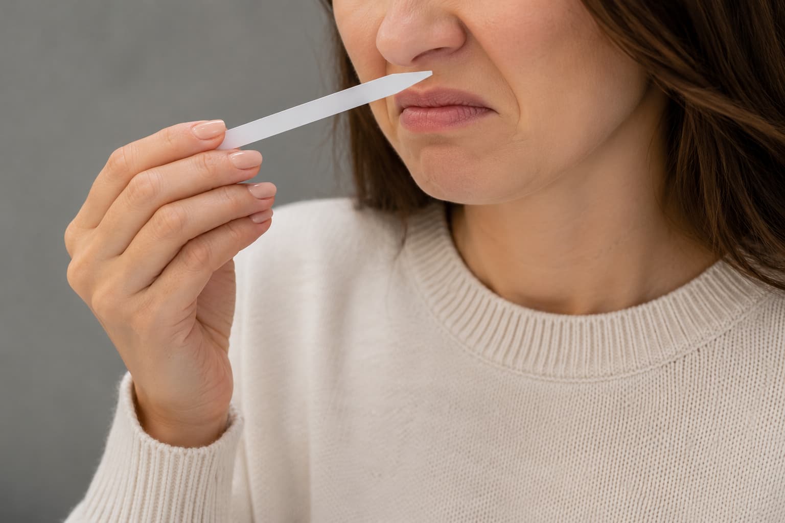 Smelling a fragrance testing strip to check whether a perfume's scent seems off, a simple way to catch a possible fake