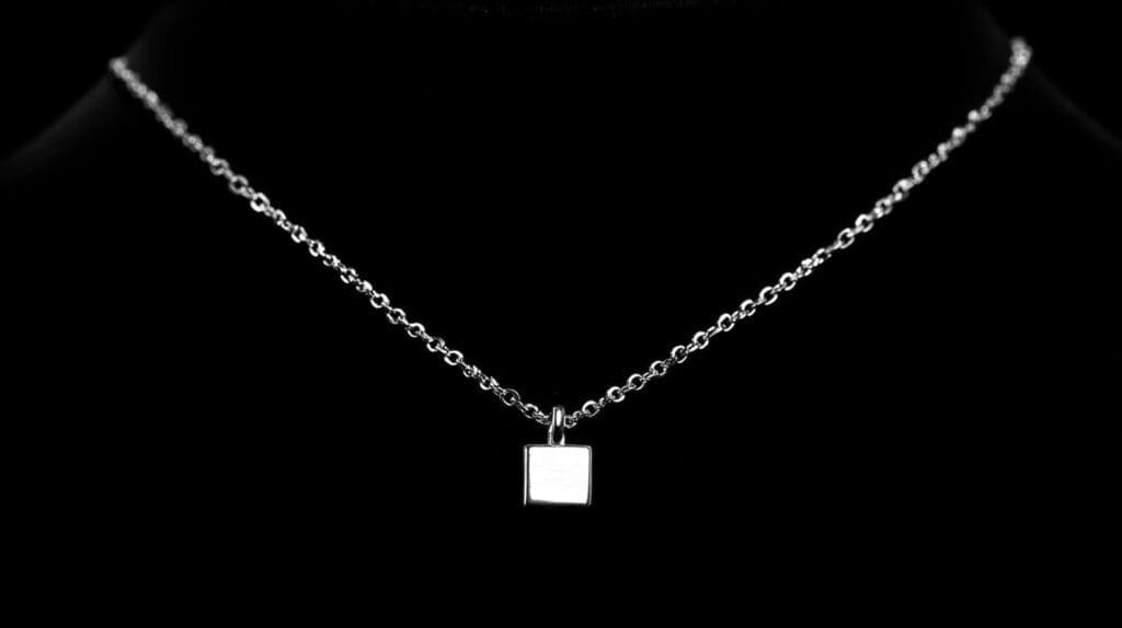 Minimalist fine silver square pendant necklace displayed on a sleek chain against a black background.