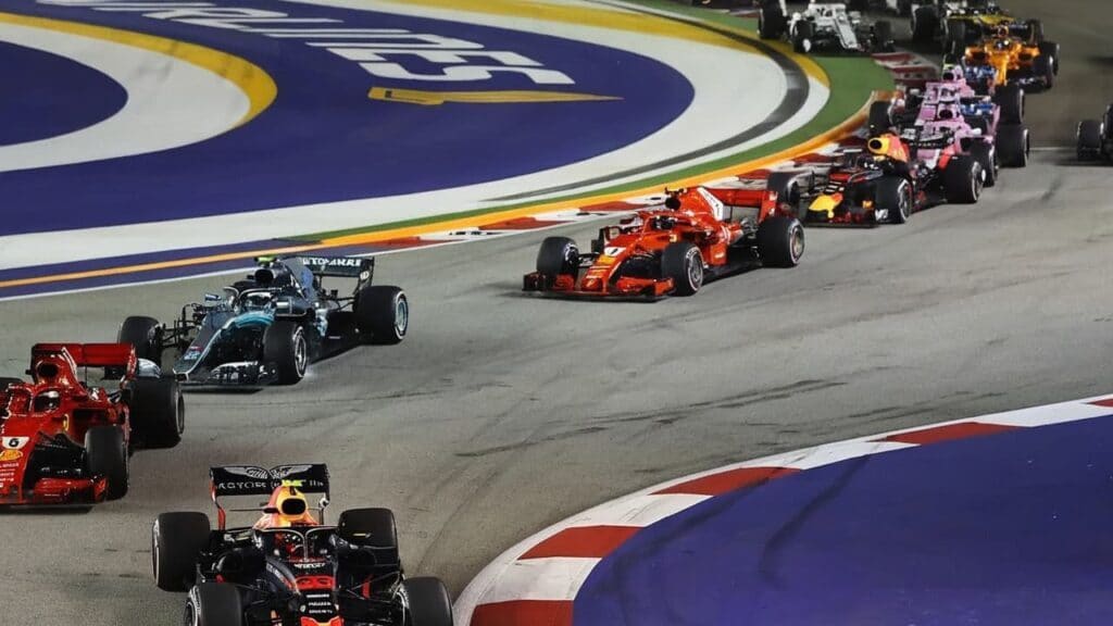 Formula 1 cars racing through turn at Singapore Grand Prix night race showing Ferrari Mercedes Red Bull teams competing on illuminated street circuit