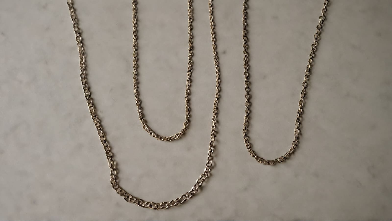 Three gold chain necklaces of different lengths laid on marble