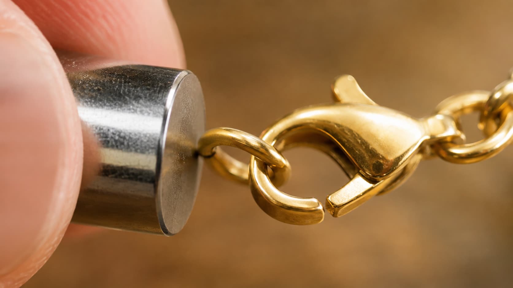 Magnet held against a gold necklace clasp to check for a magnetic reaction