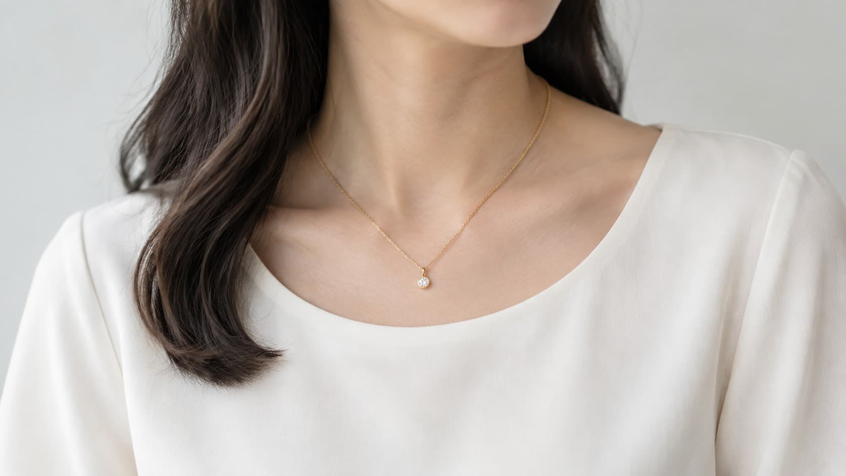 Woman wearing a thin gold pendant necklace with a white blouse for a business casual outfit
