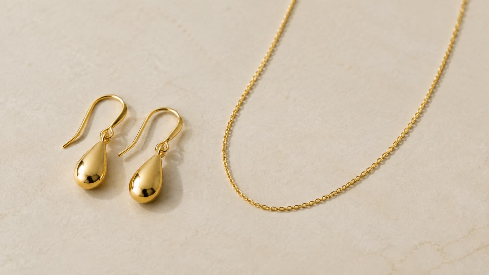Gold teardrop drop earrings next to a delicate thin chain necklace