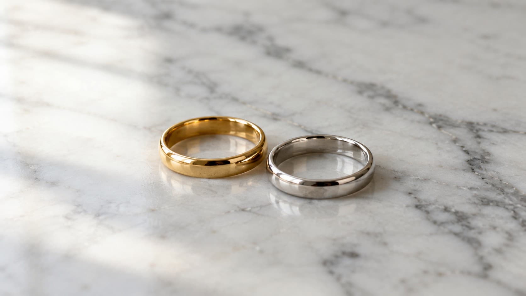Gold ring and silver ring placed side by side on a marble surface