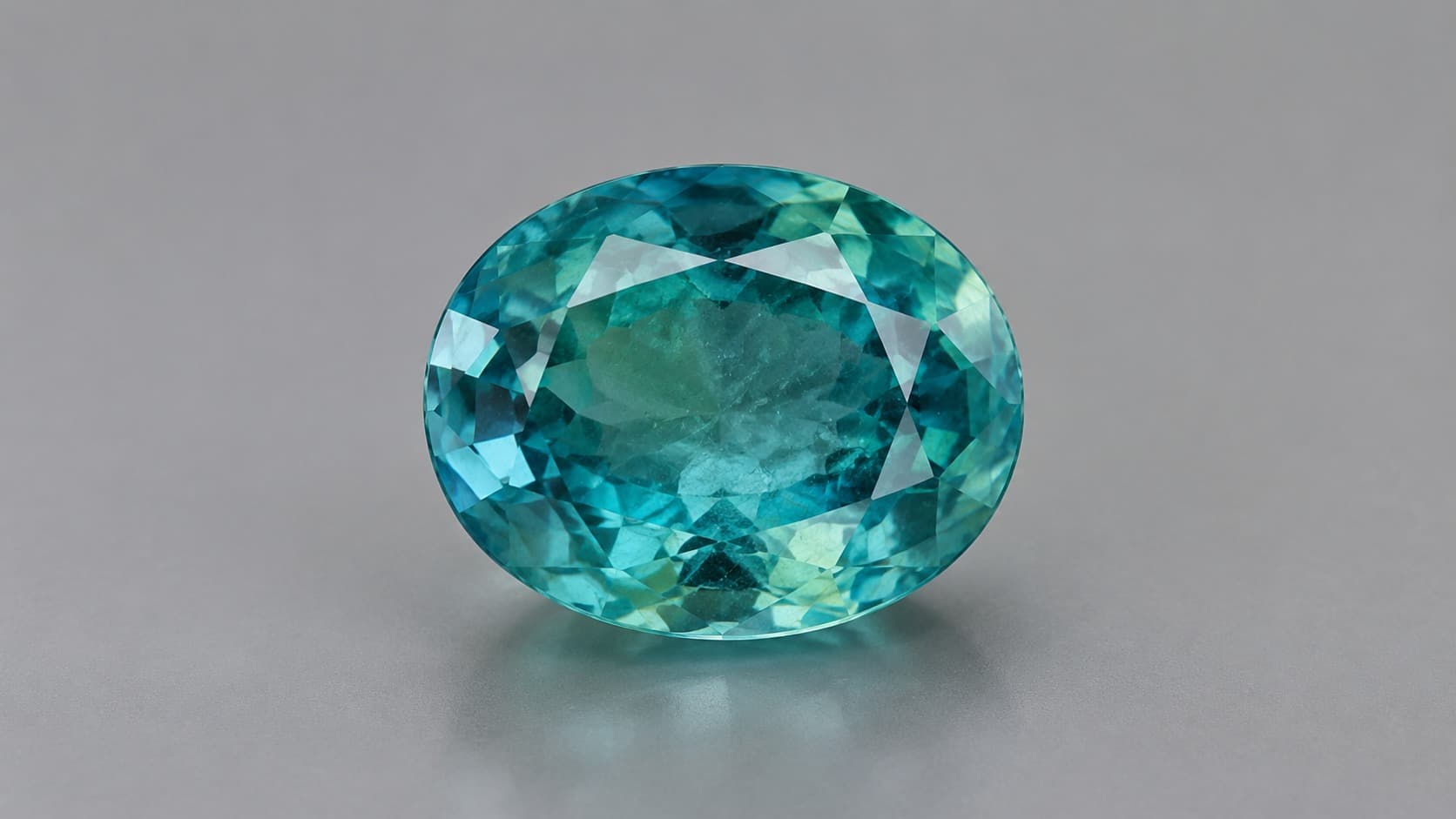 Faceted blue-green grandidierite gemstone on a neutral gray background