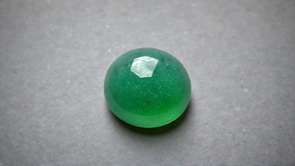 Smooth, polished green aventurine cabochon gemstone with a glossy finish, placed on a neutral-toned surface.
