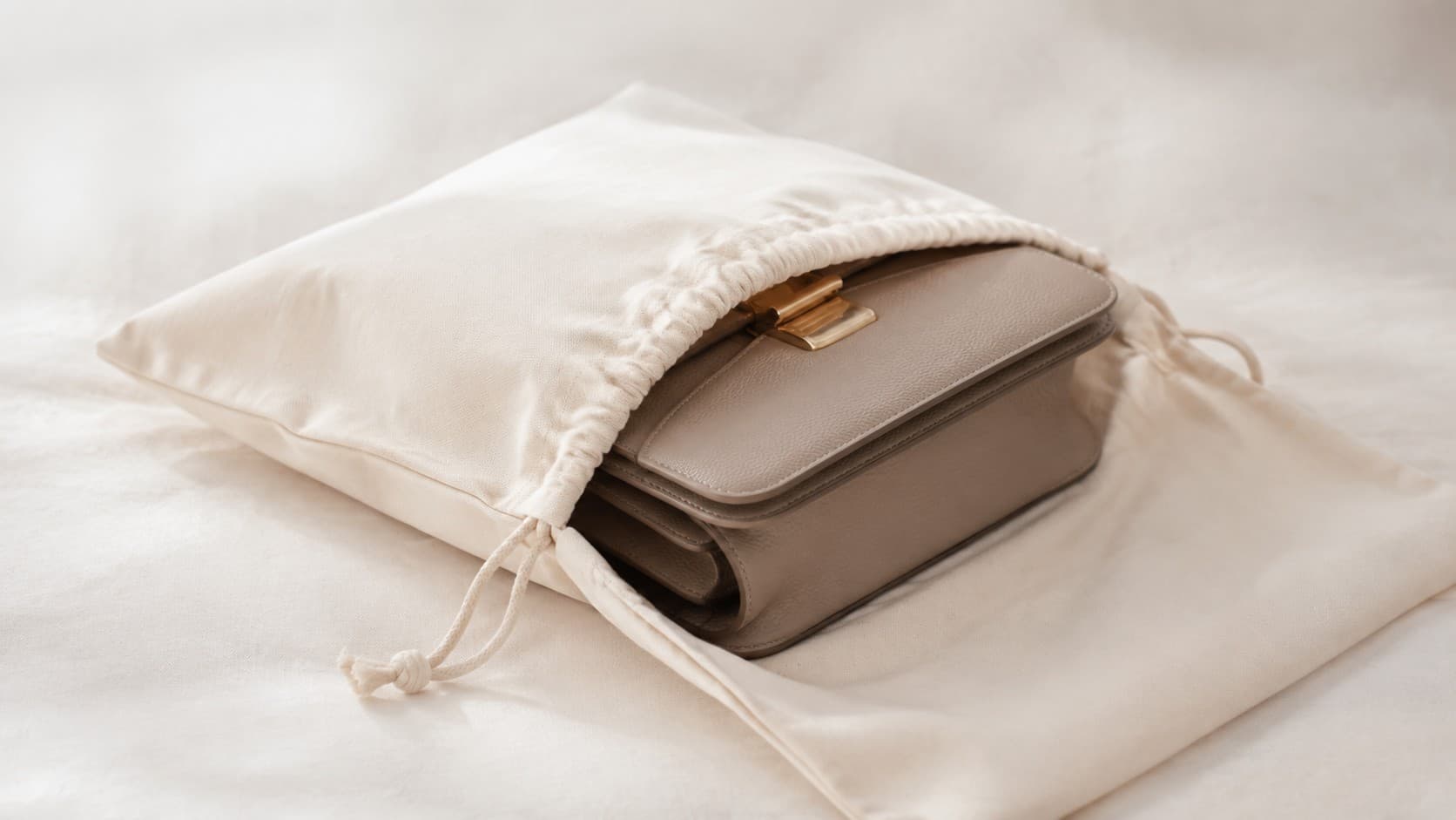 Structured handbag being placed into a breathable cotton dust bag