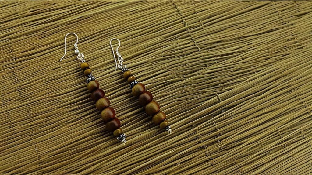 A pair of handcrafted wooden beaded earrings with silver accents displayed on a woven mat, combining rustic charm with elegant design.
