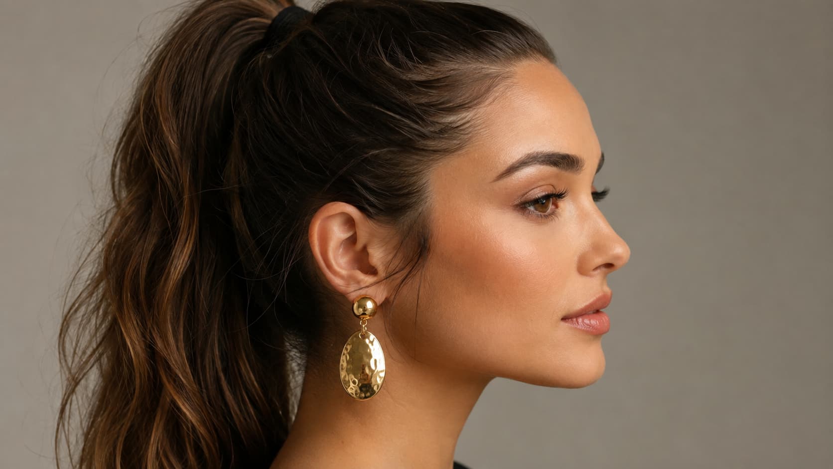 Woman with a high ponytail wearing gold statement drop earrings