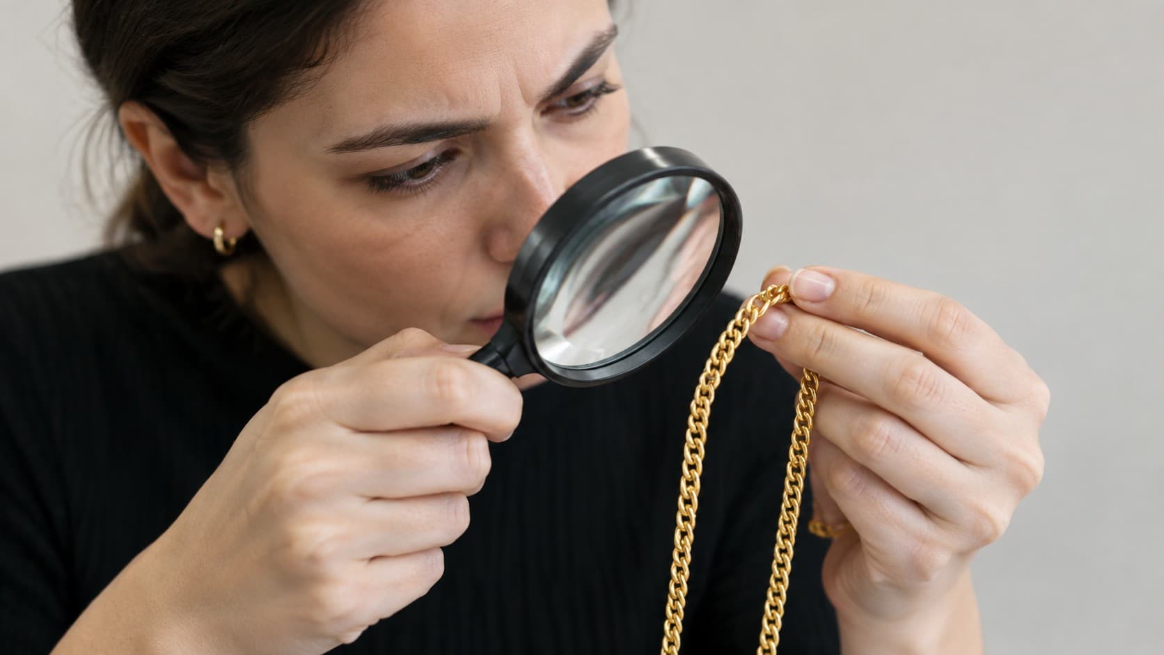 Inspecting a gold chain with a magnifying glass for signs of underkarating fraud