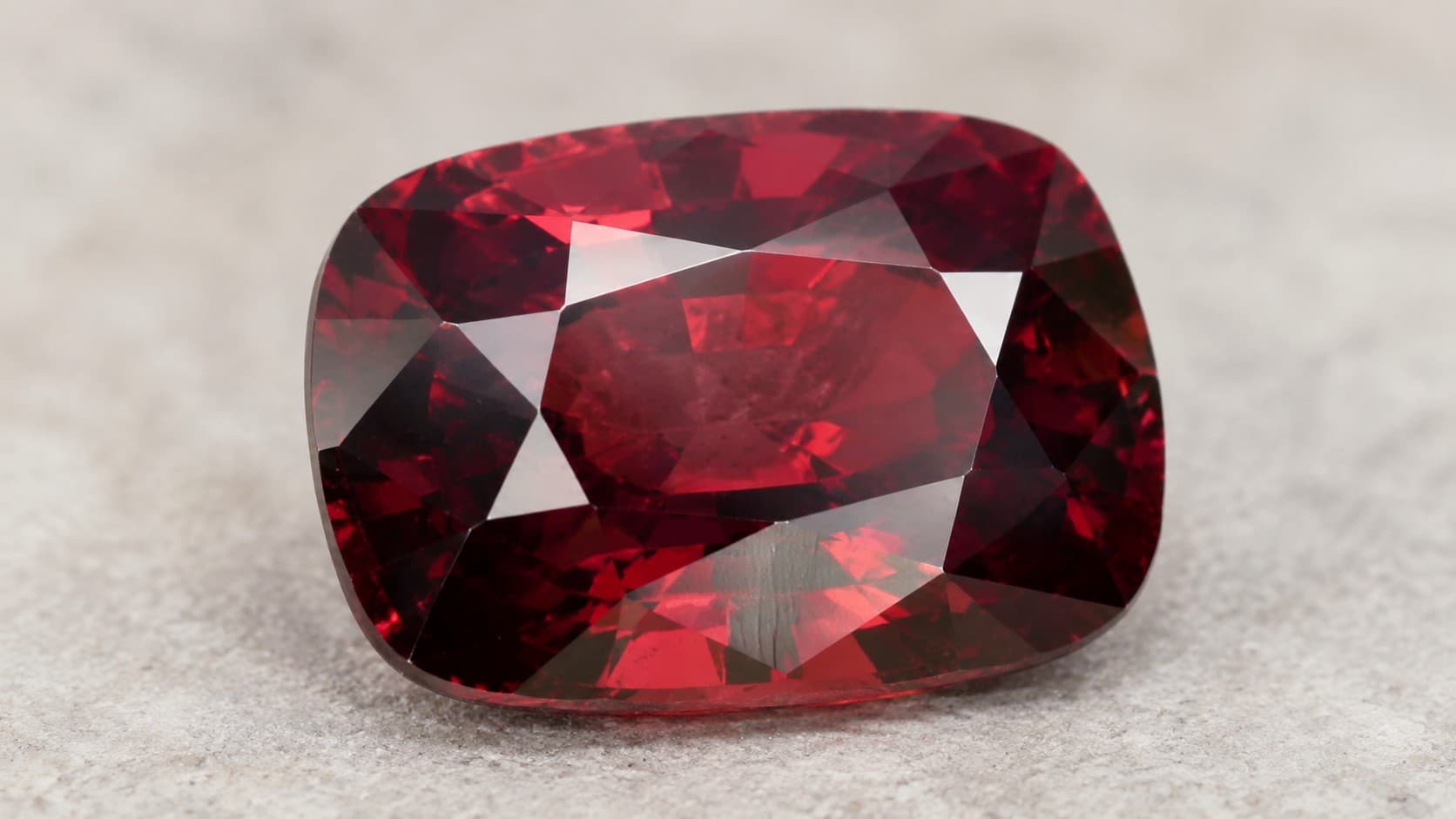 Cushion cut deep red garnet gemstone, January's birthstone, on a light grey stone surface