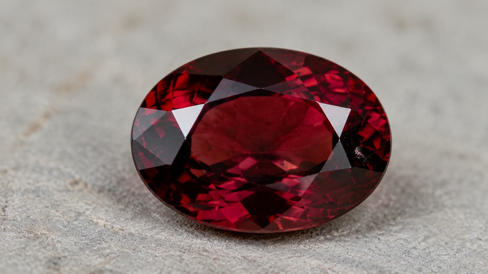 Oval cut deep red garnet gemstone, January's birthstone, on a light grey stone surface