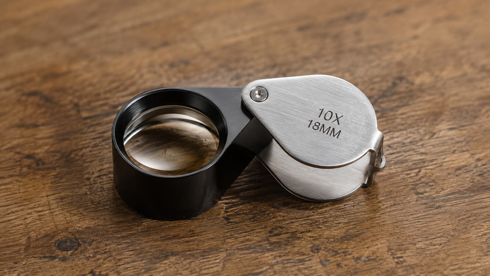 A 10x jeweler's loupe with an 18mm lens, folded closed on a wooden surface
