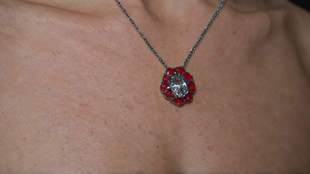 Silver necklace with red gemstone pendant resting on chest skin showing jewelry contact area