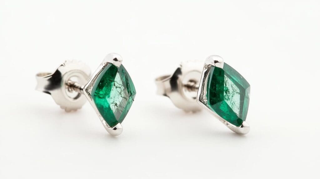A pair of elegant kite-cut green emerald stud earrings set in white gold, highlighting their unique geometric cut and natural inclusions.