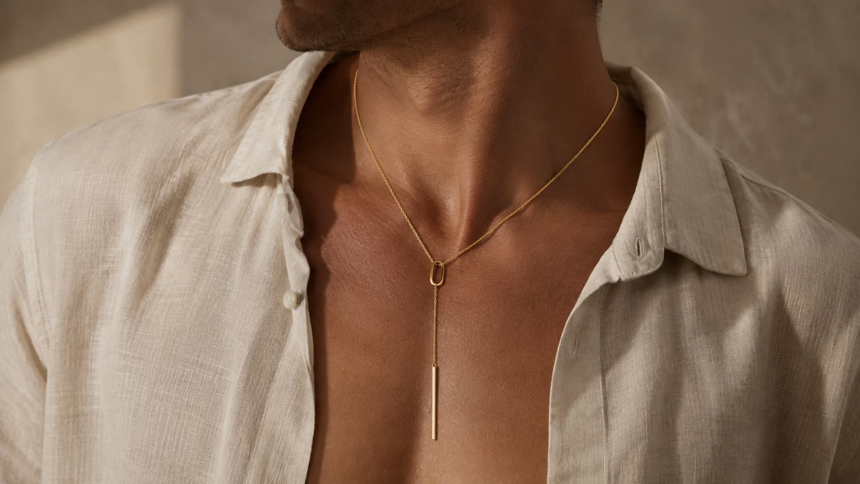 Gold lariat necklace worn by a man with an open linen shirt