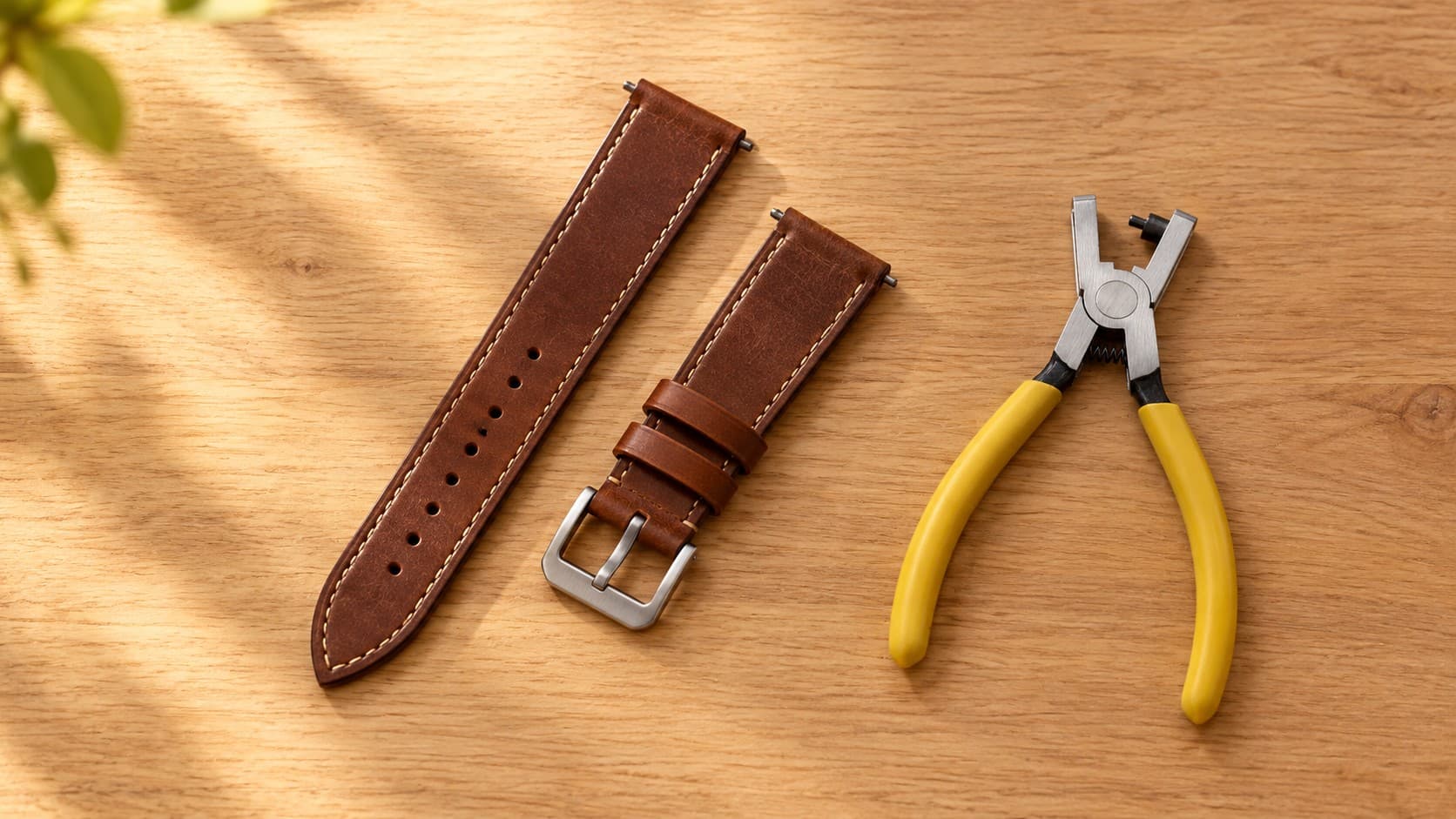 Brown leather watch strap next to a hole punch plier tool for resizing