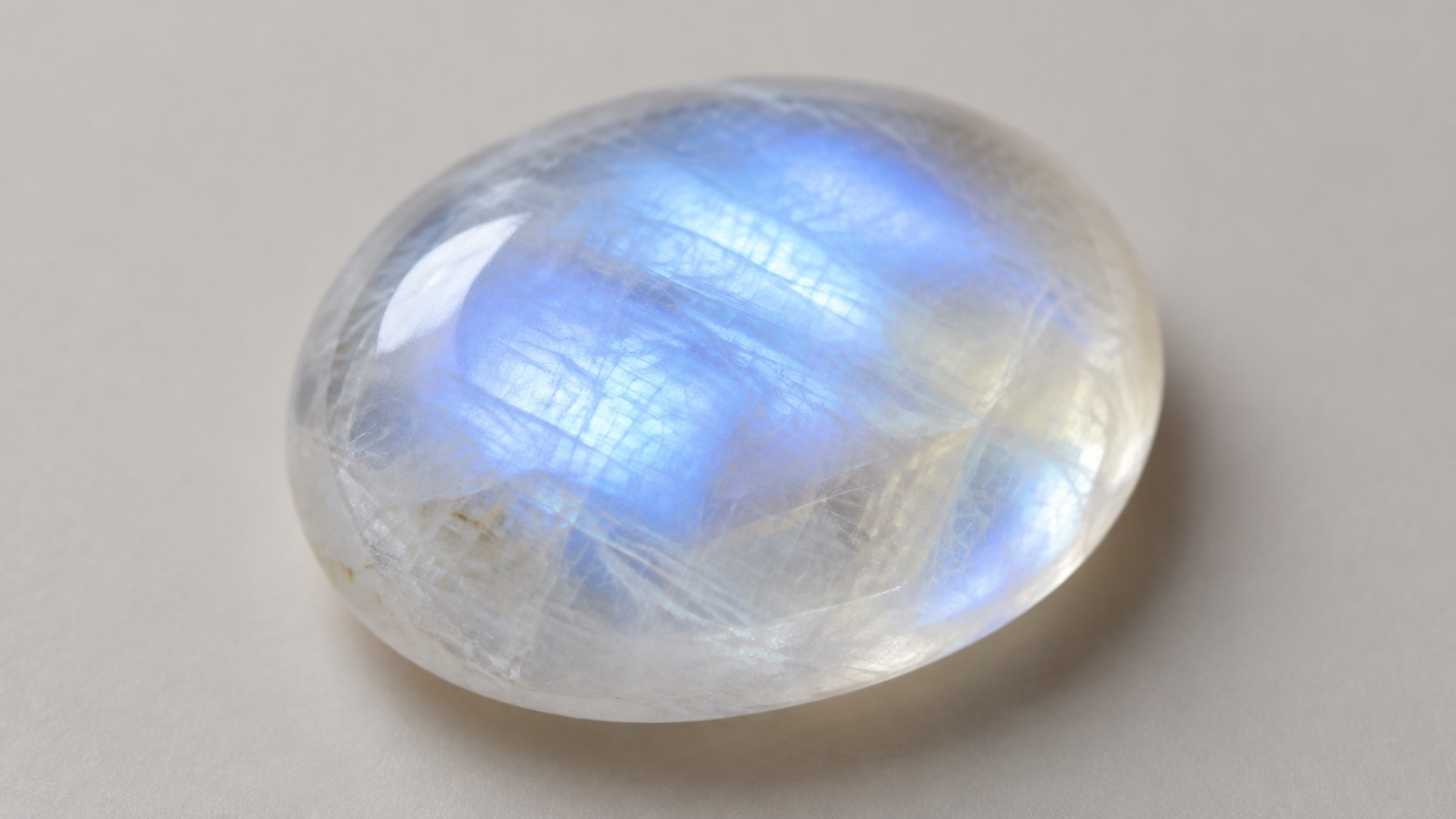Smooth cabochon moonstone with a blue glow on a neutral background